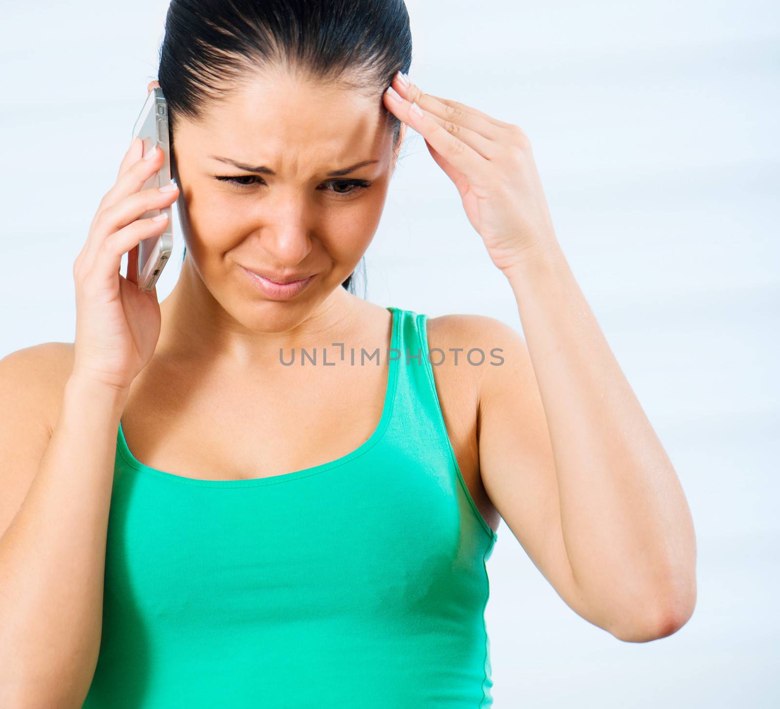 sad young brunette woman holding her head and talking by mobile phone at home
