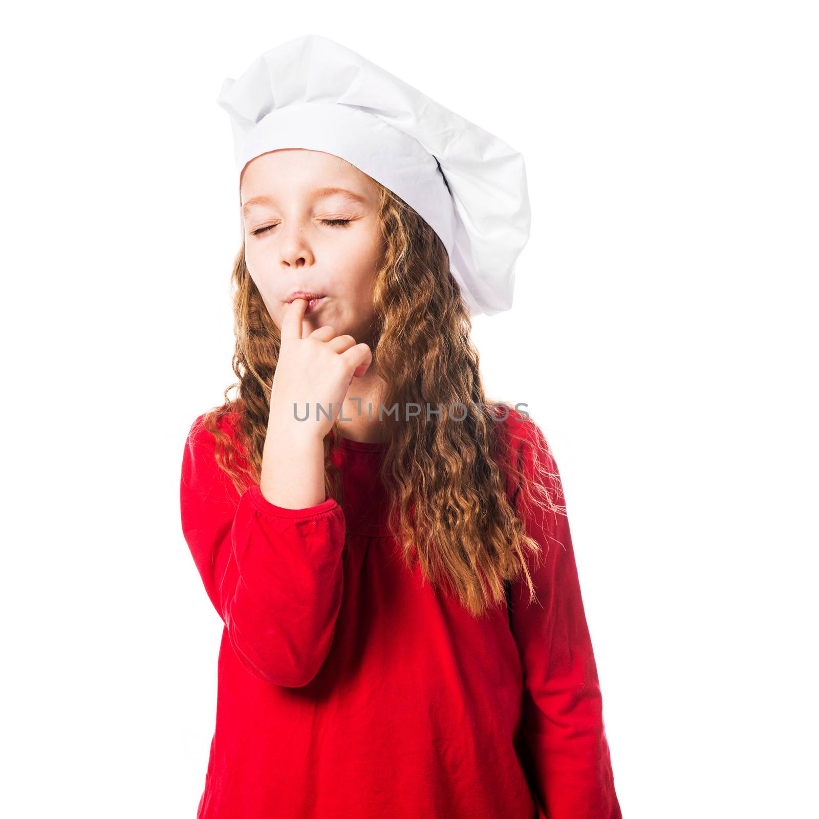 little girl in chef hat licks a finger with eyes closed on white background