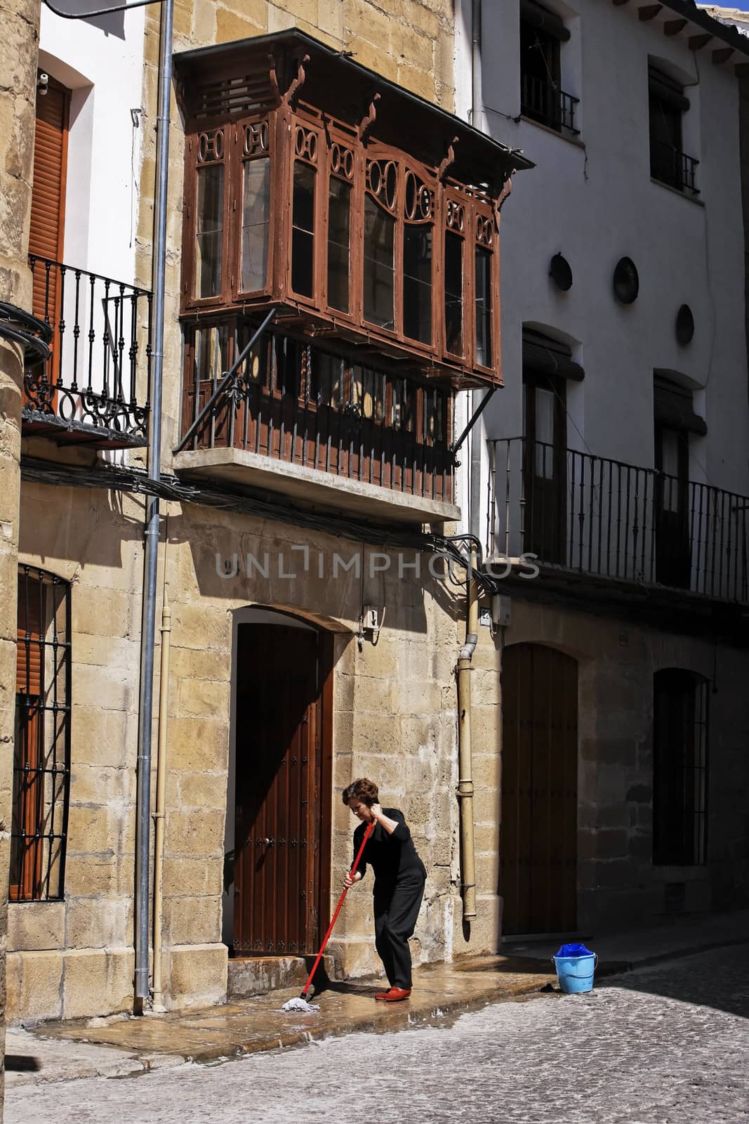 House and traditional balcony in Ubeda, woman cleaning the entrance on a sunny day, Ubeda, Jaen province, Andalusia, Spain