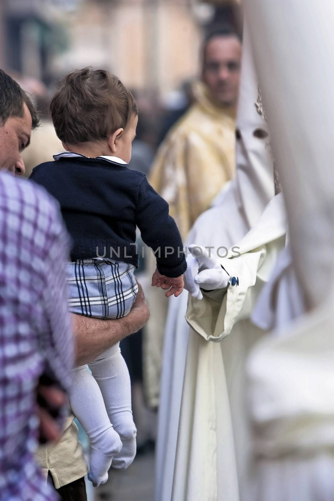 penitent touches the finger of the hand of a child during a Holy week procession, Linares, Jaen province, Andalucia, Spain