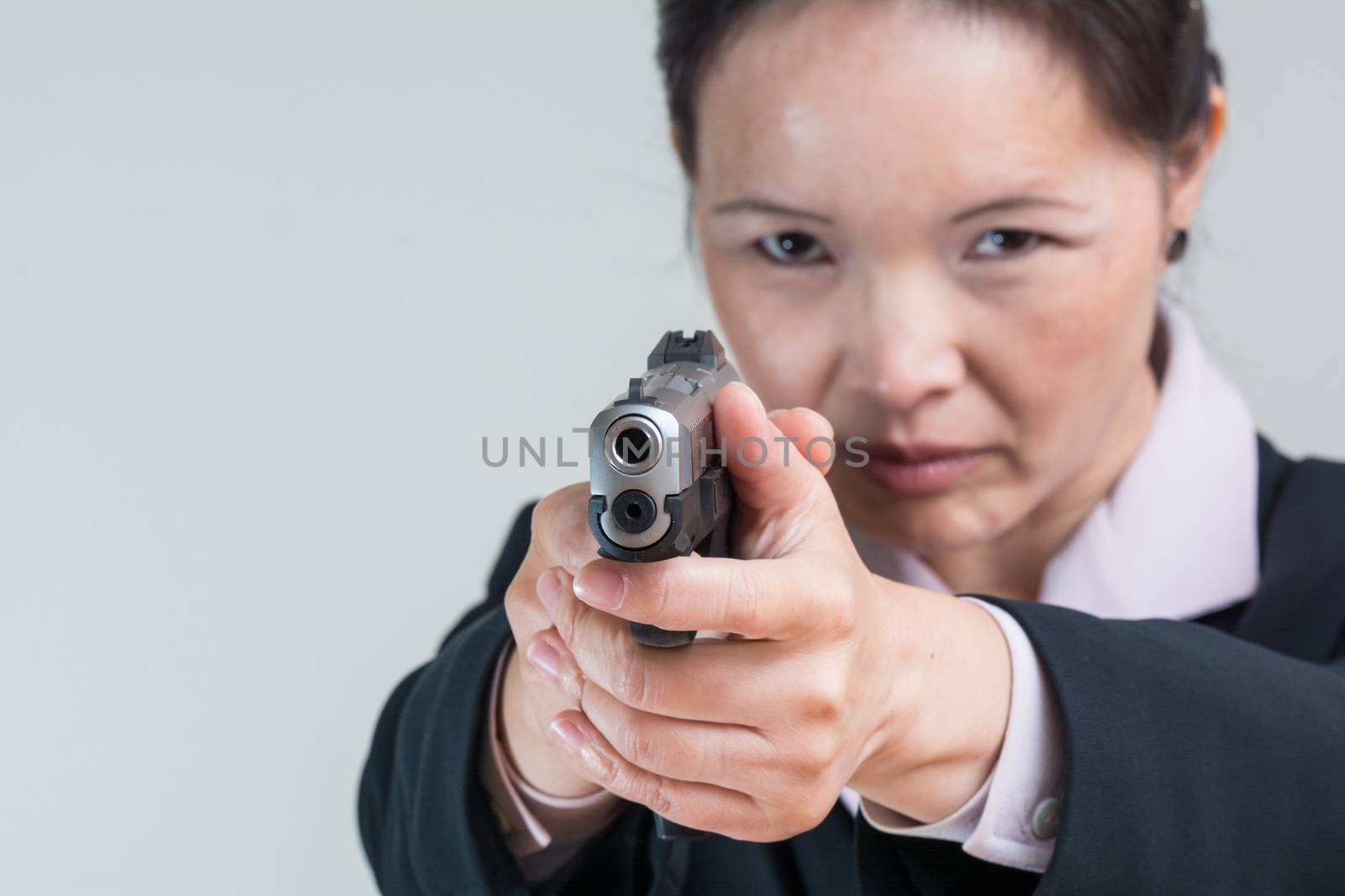 Close up portrait of woman in business suit aiming a hand gun at you
