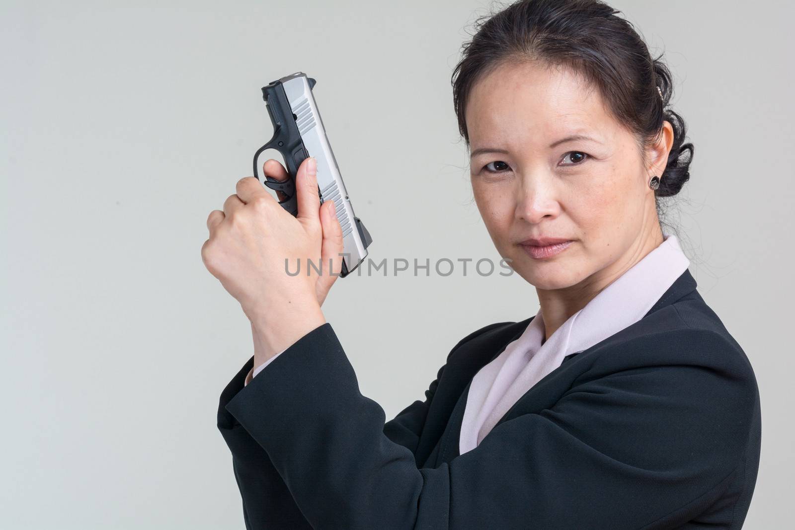 Portrait of woman in business suit holding a hand gun with agent pose on grey background
