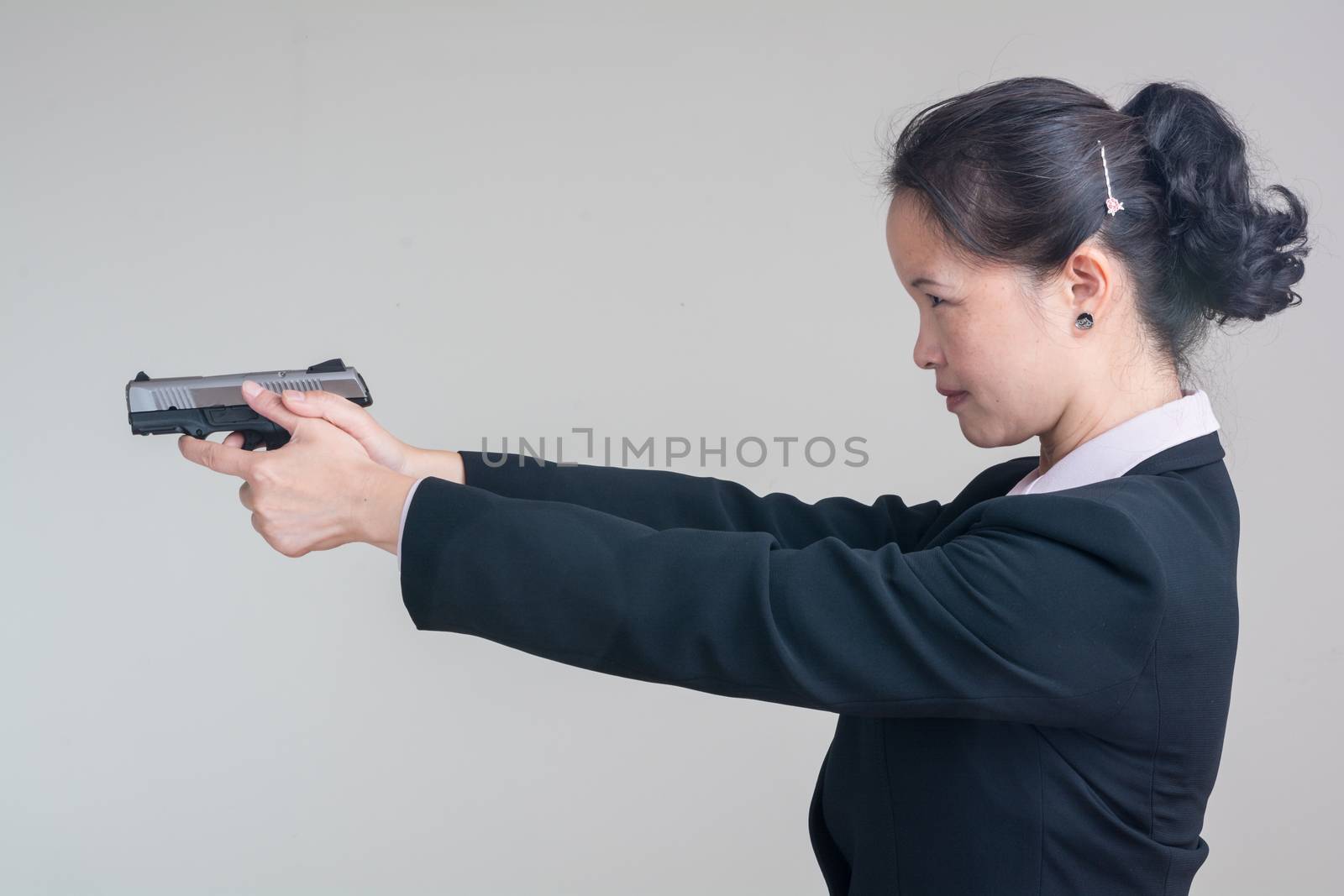 Portrait of woman in business suit aiming a hand gun on grey background