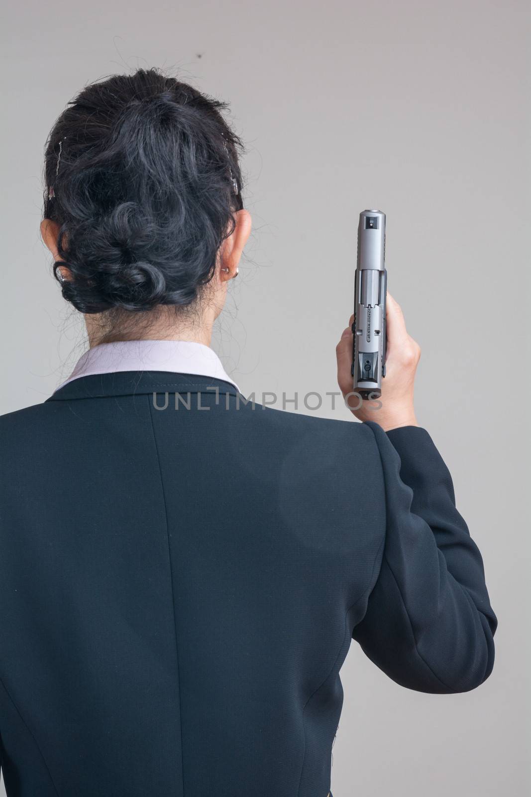 Back of woman in business suit holding a hand gun pointing up