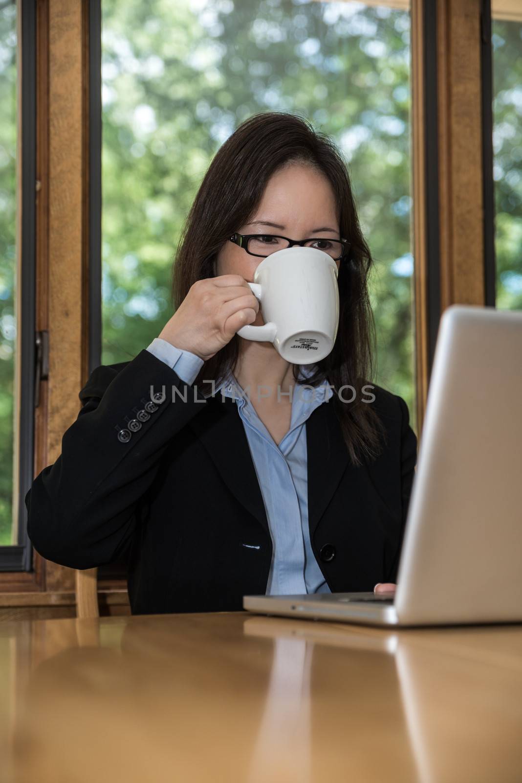 Woman in business suit with laptop on desk and drinking coffee in front of a window