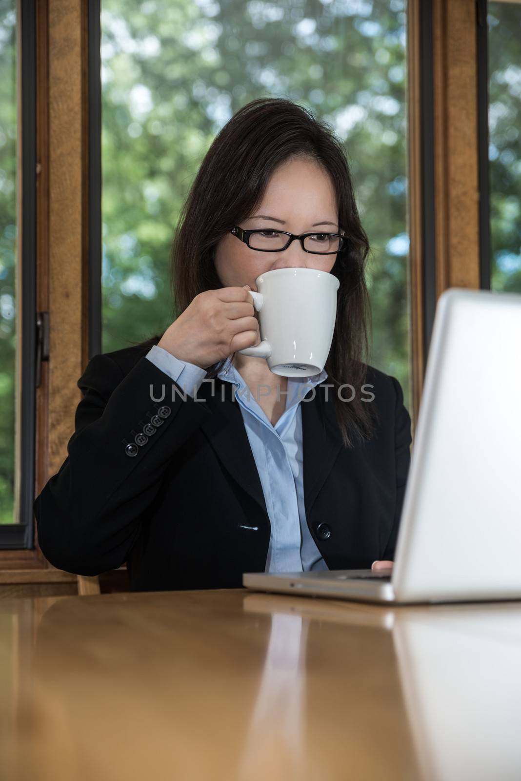 Woman in business suit with laptop on desk and drinking coffee in front of a window