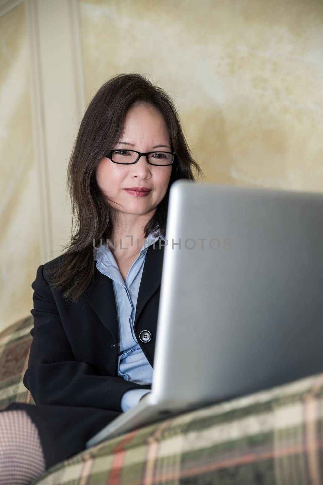 Woman on sofa on laptop by IVYPHOTOS