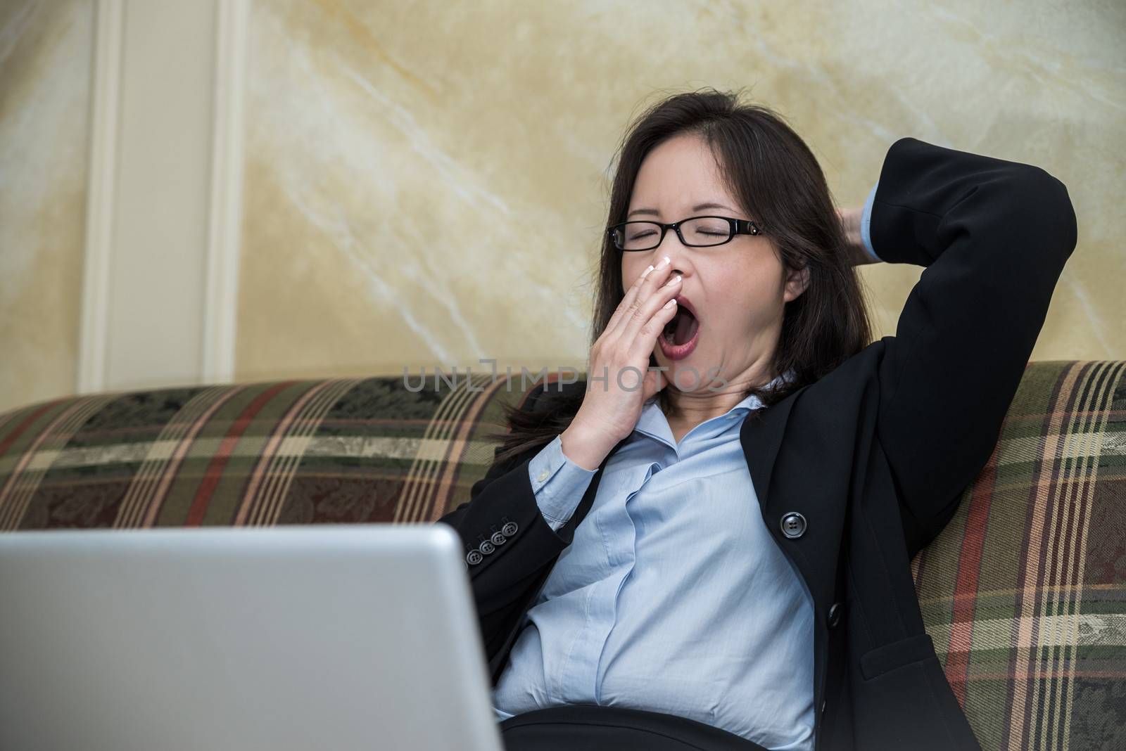 Woman in business suit feeling tired and yawning on sofa with labtop