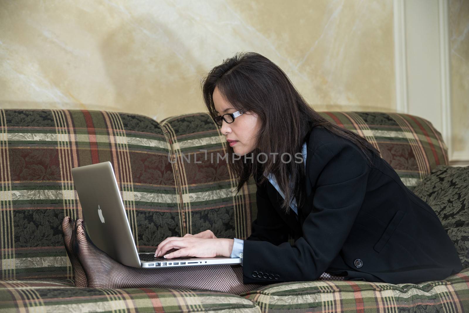 Woman in business suit relaxing on sofa and typing on laptop at home 
