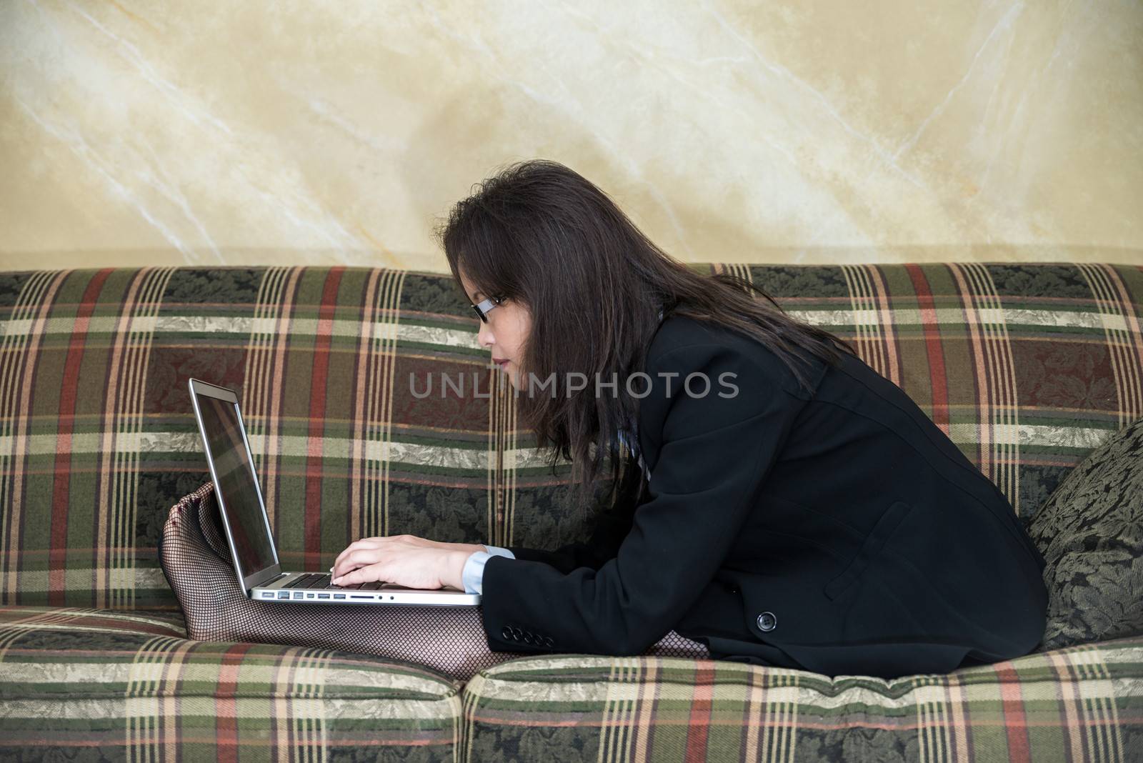 Woman typing on laptop on sofa by IVYPHOTOS