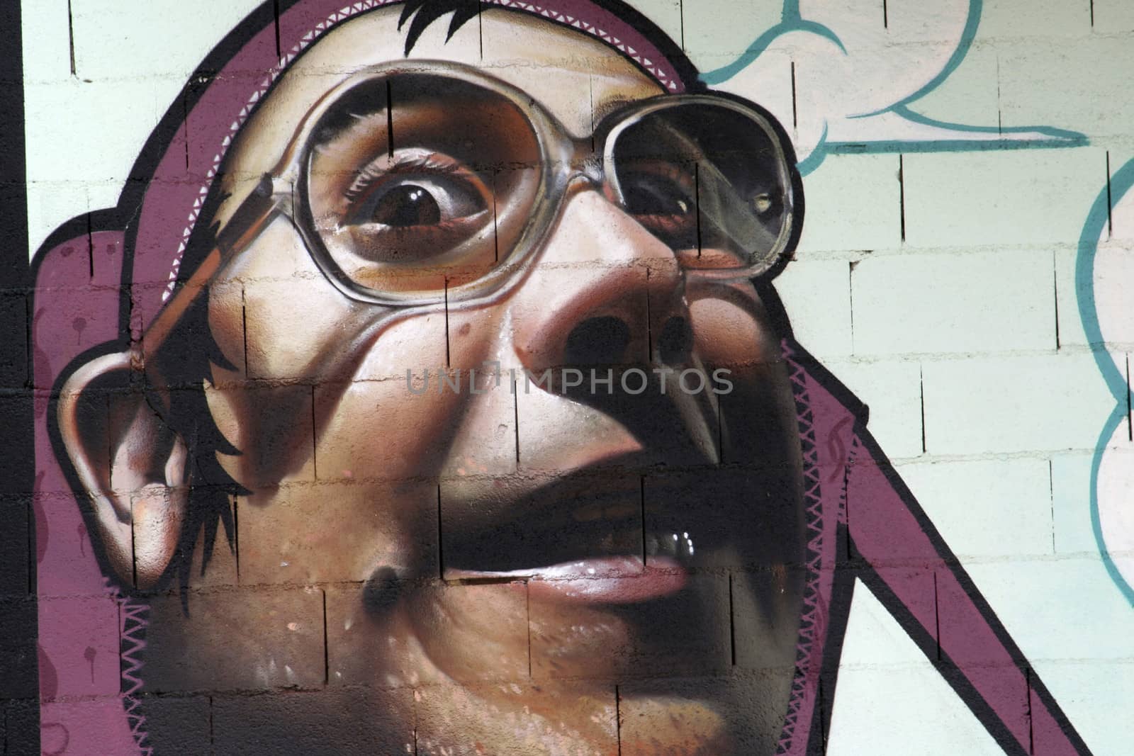 Graffiti of a young man with glasses smiling painted with bright colors on a wall, Andalucia, Spain