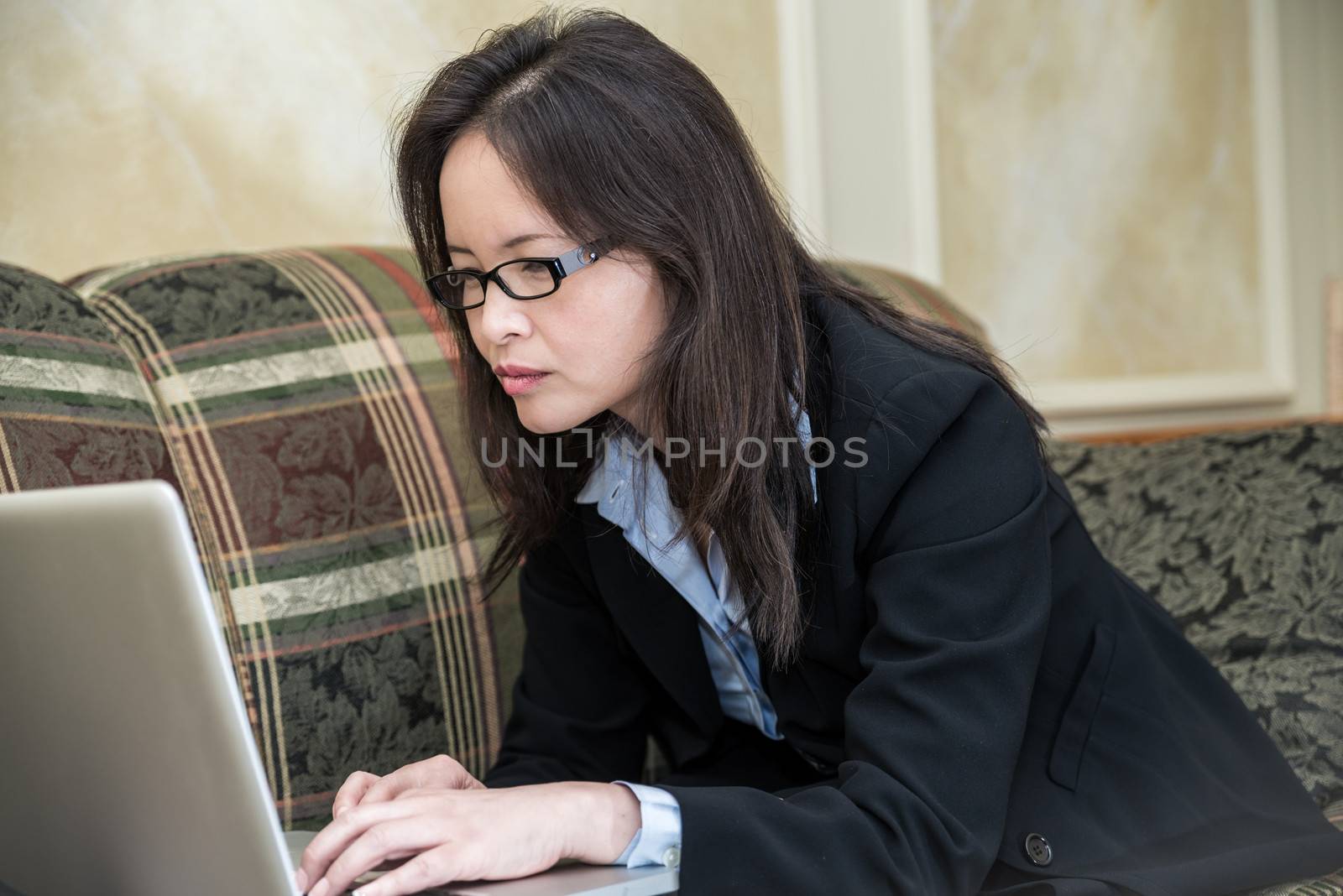 Woman in business suit relaxing on sofa and typing on laptop at home 