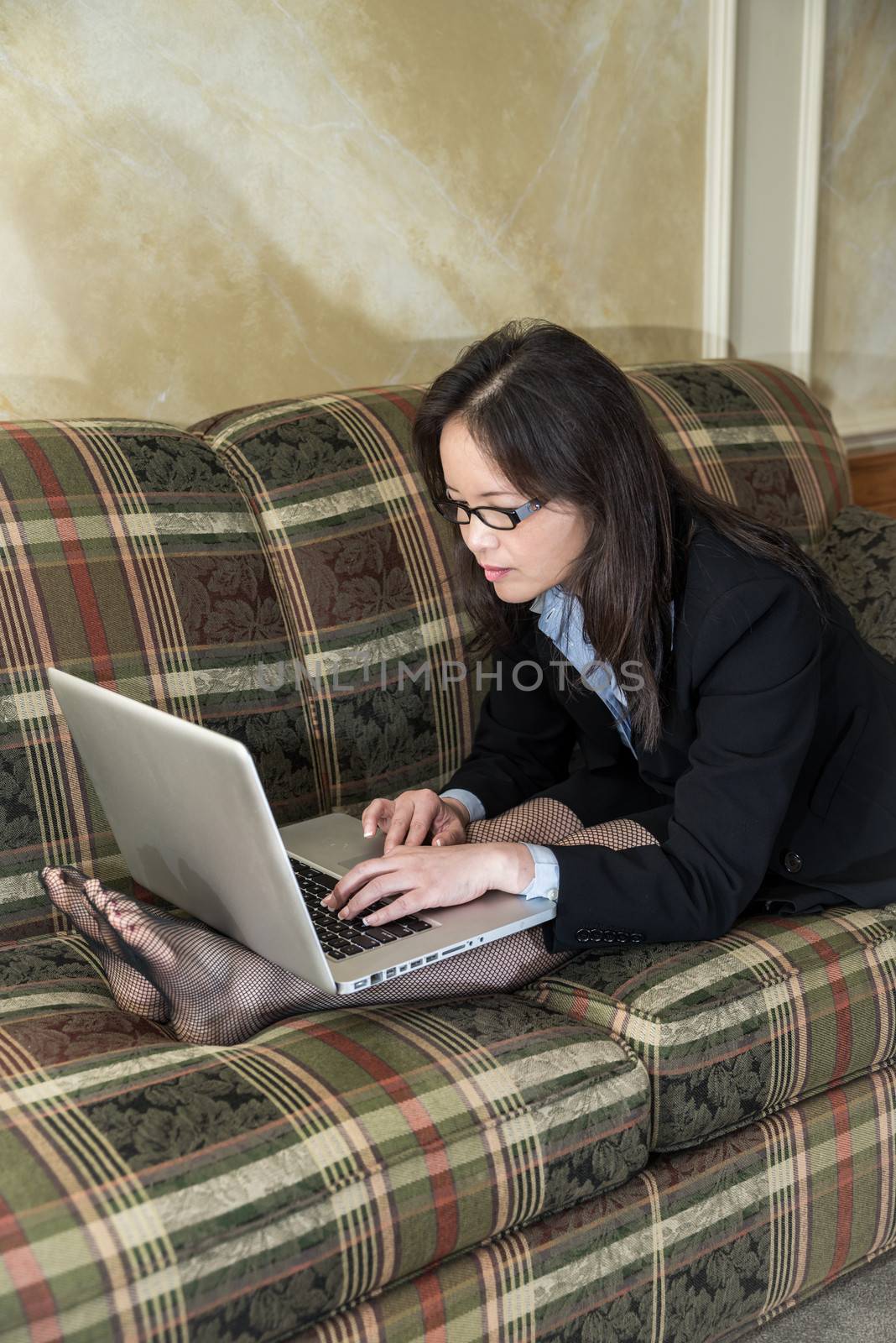 Woman typing on laptop on sofa by IVYPHOTOS