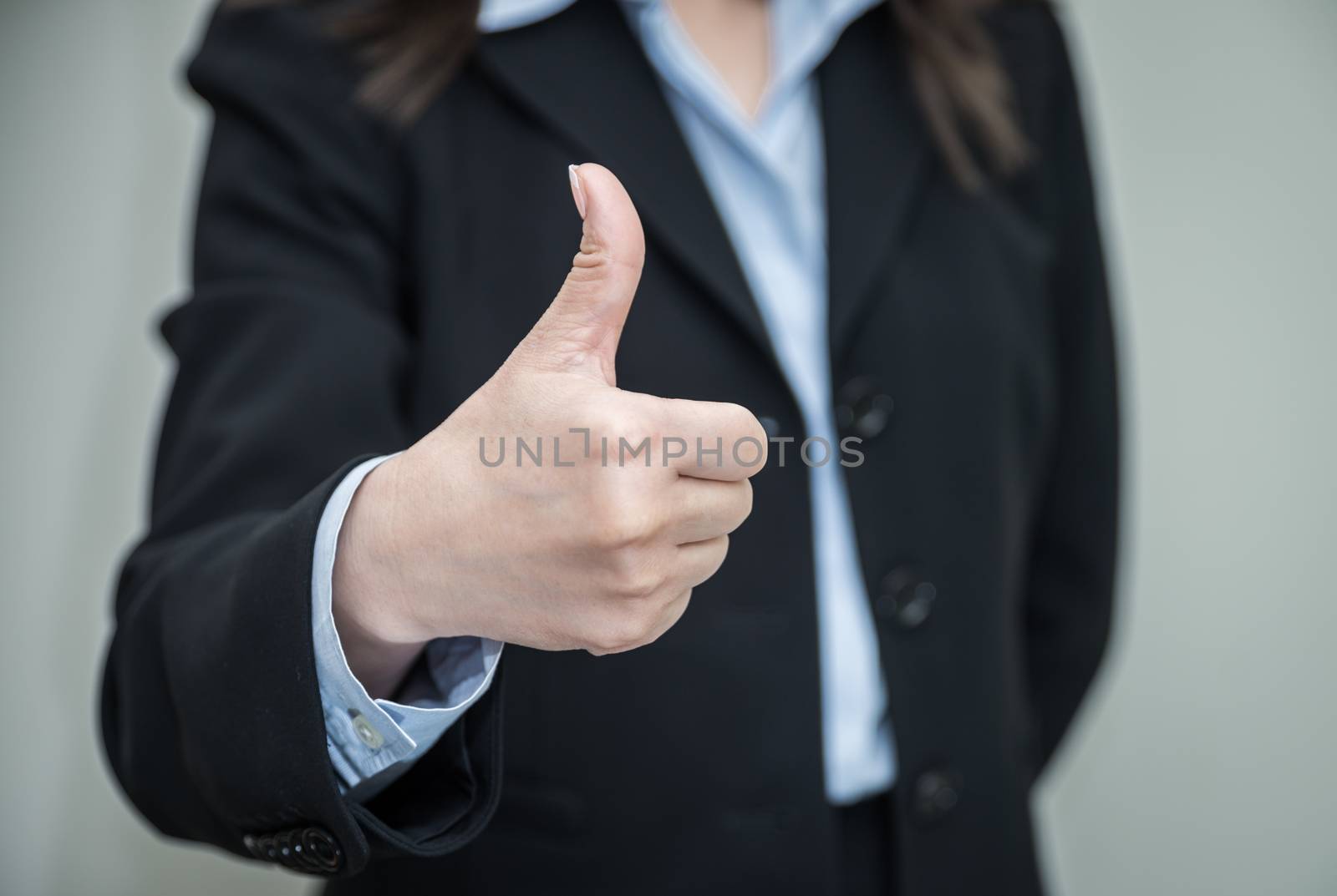 Professional woman in business suit giving thumbs up in approval on grey background 