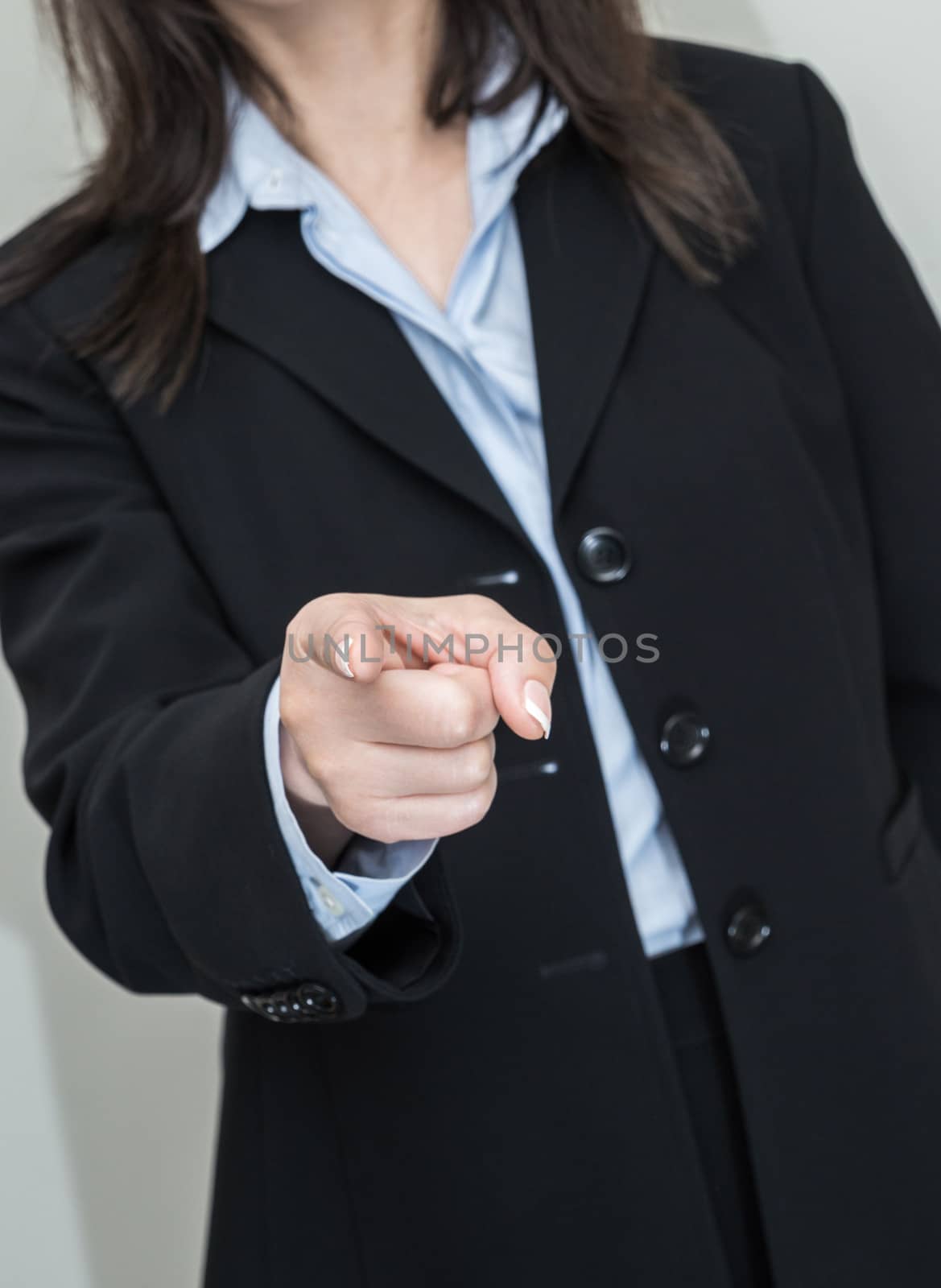 Professional woman in business suit pointing at you with one finger on grey background 