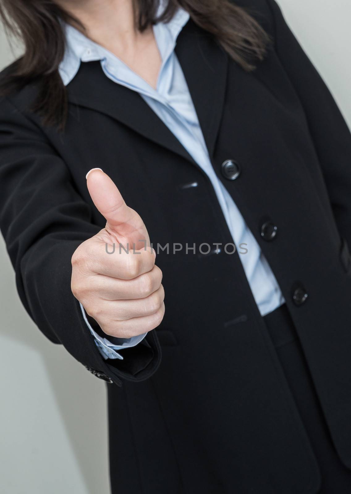 Professional woman in business suit giving thumbs up in approval on grey background 