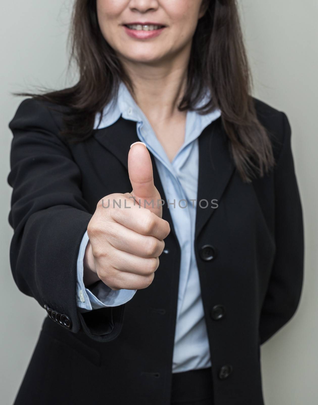 Professional woman in business suit giving thumbs up in approval on grey background 