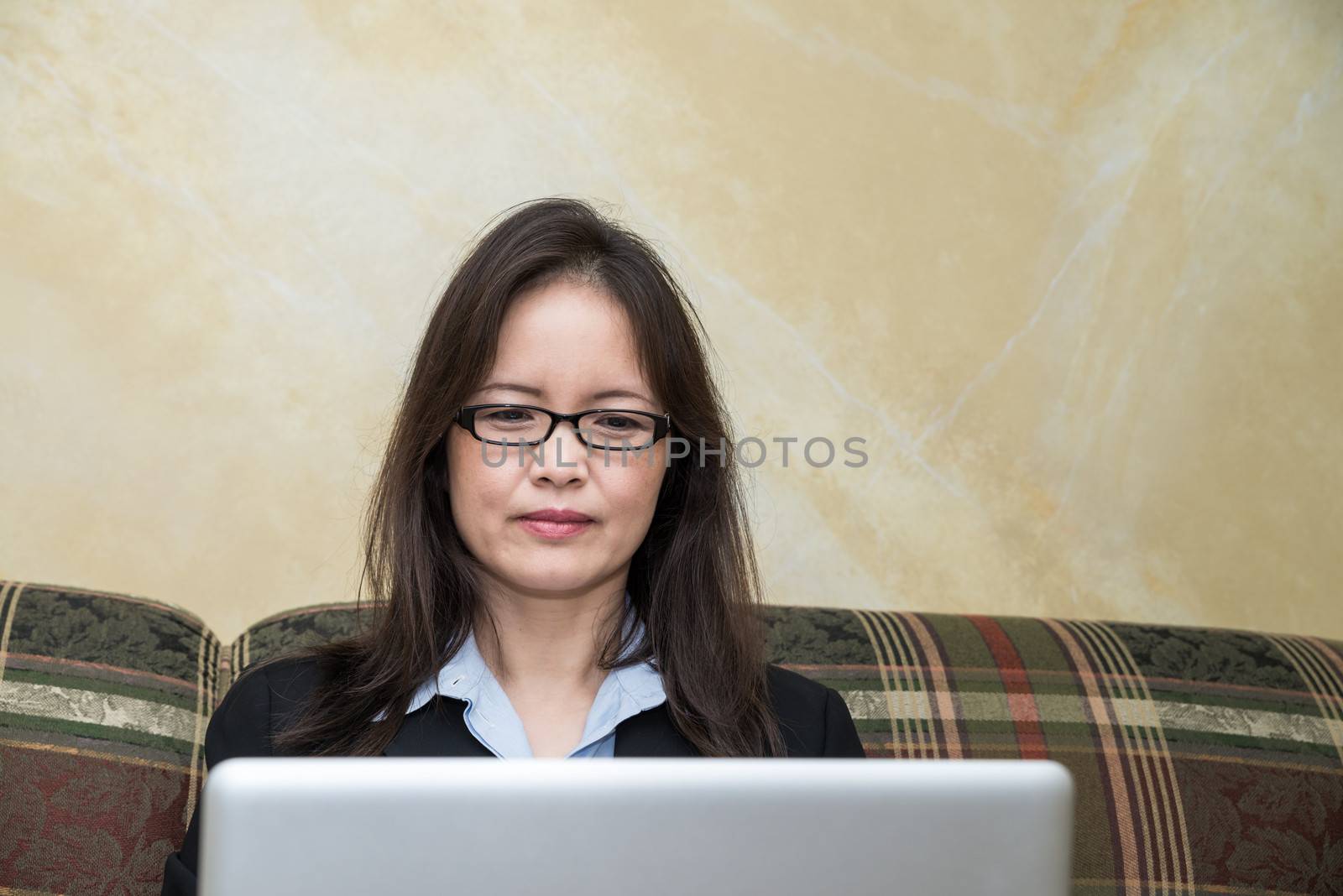 Woman with pen and laptop on sofa by IVYPHOTOS