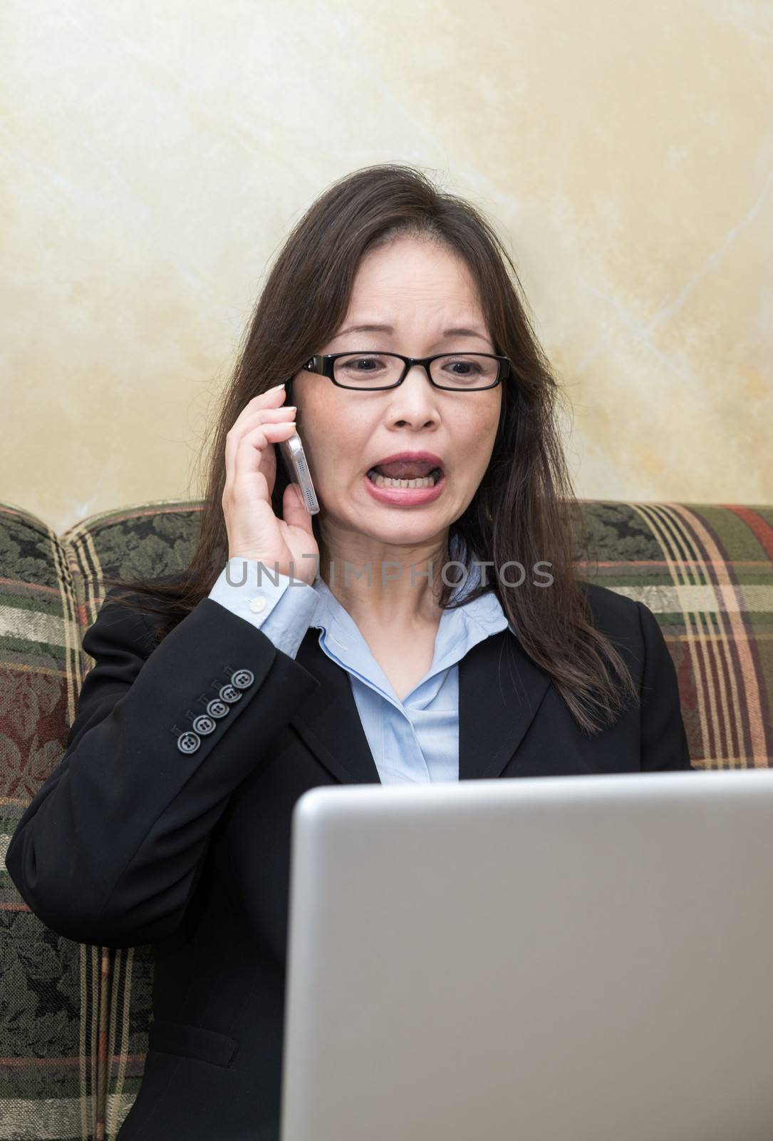 Professional woman in business suit yelling on a cell phone while looking at laptop