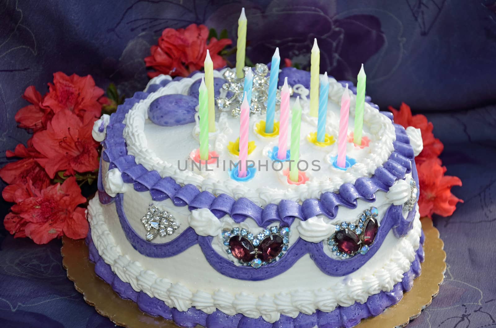 A birthday cake iced in white and purple frosting and decorated with candles and embedded gifts of jewelry