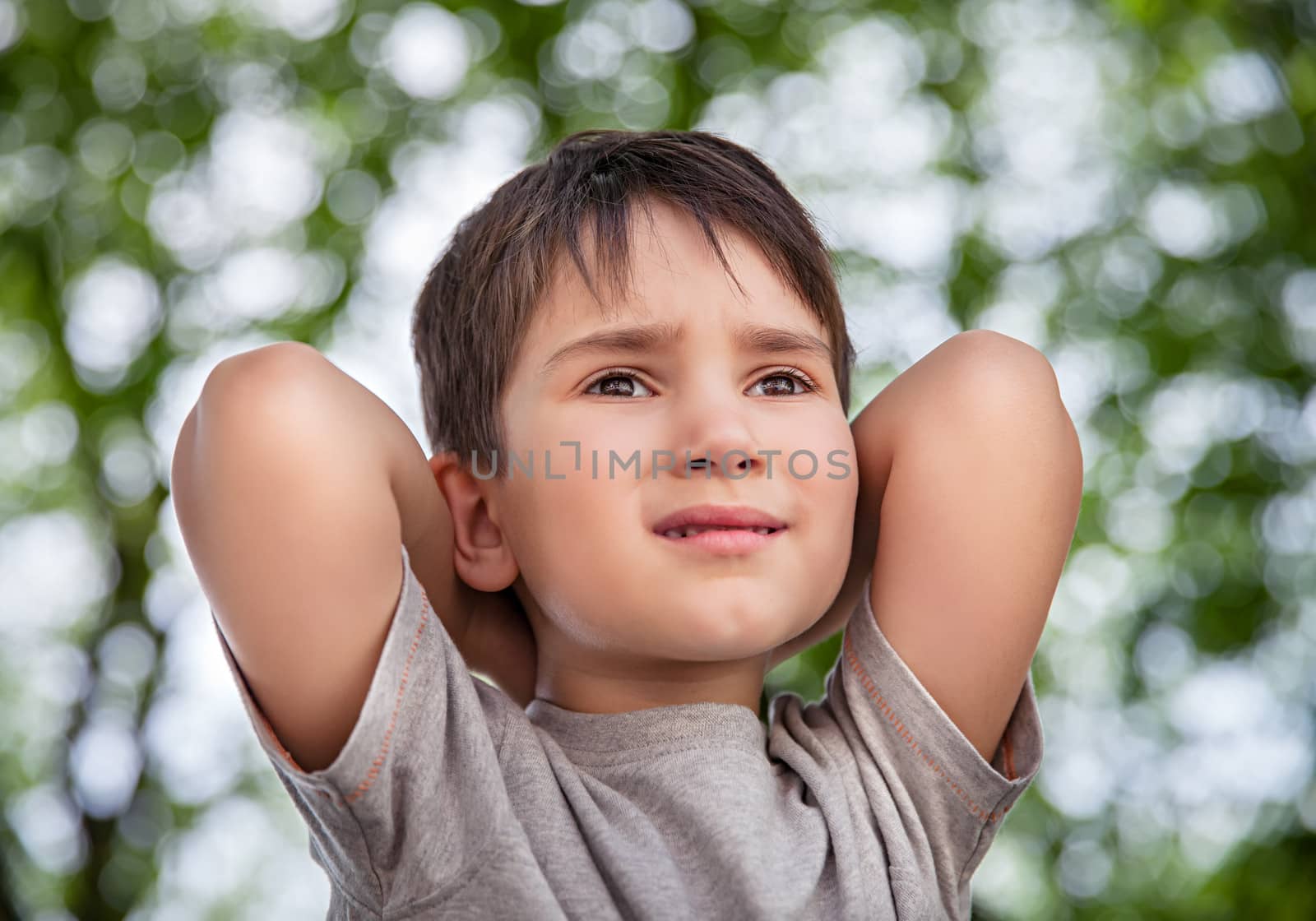 Sad little boy looking at something against blurred natural background