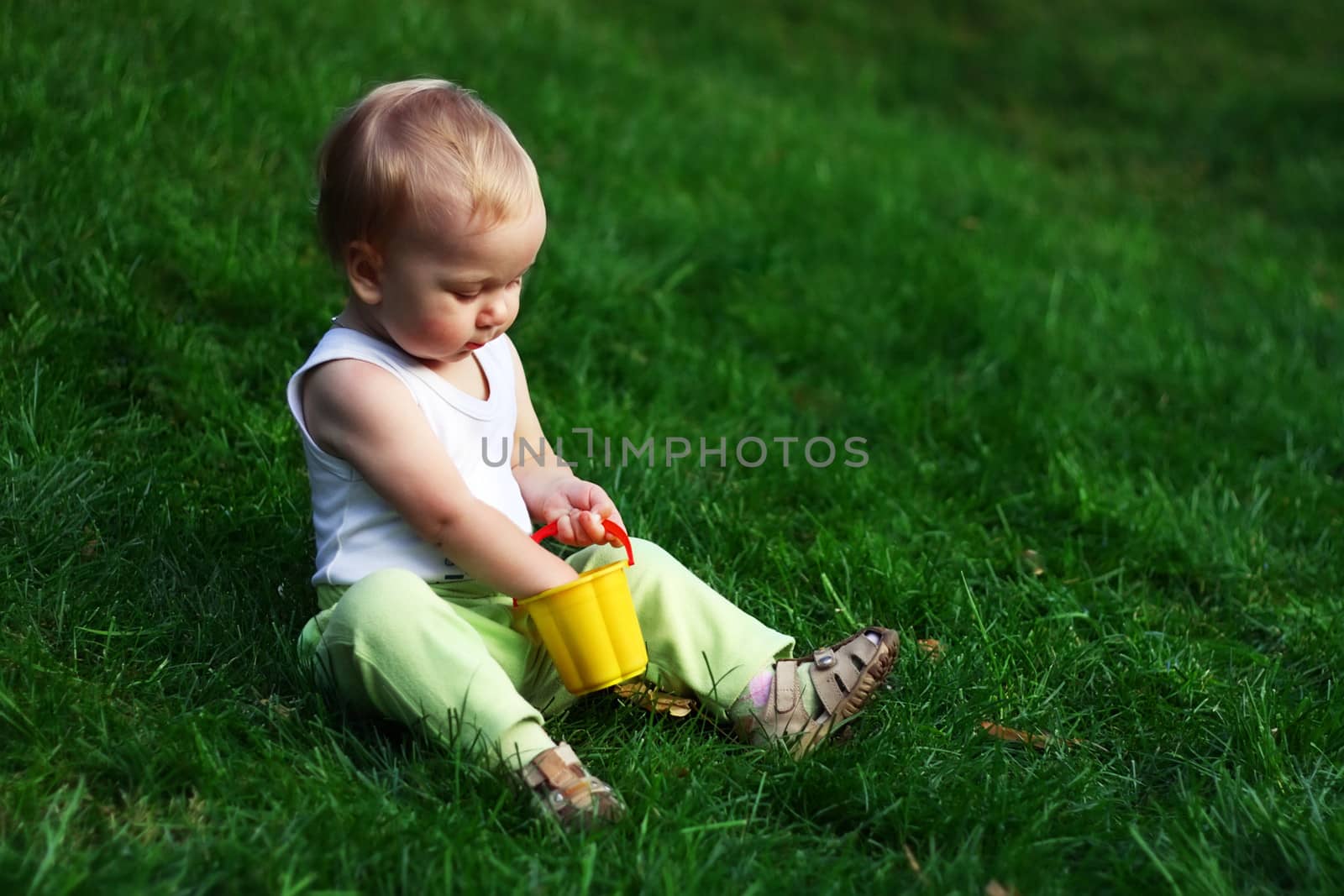Little boy with pail sits on a green grass