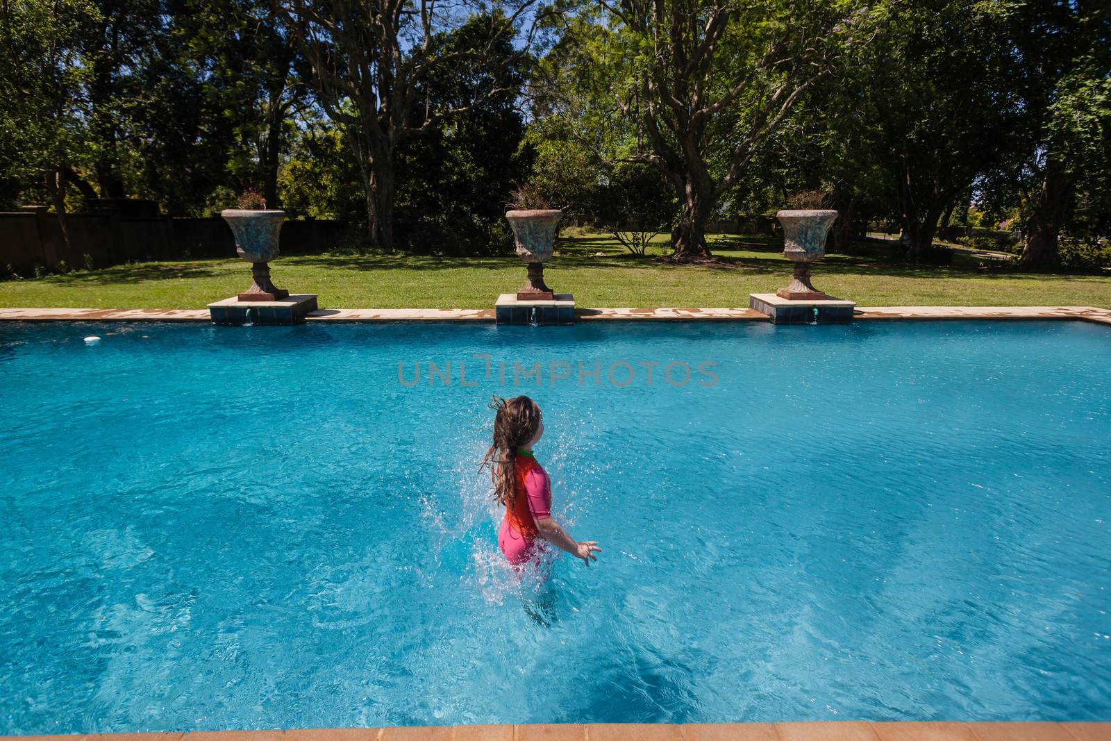 Young girl having fun jumping into summer blue swimming pool.