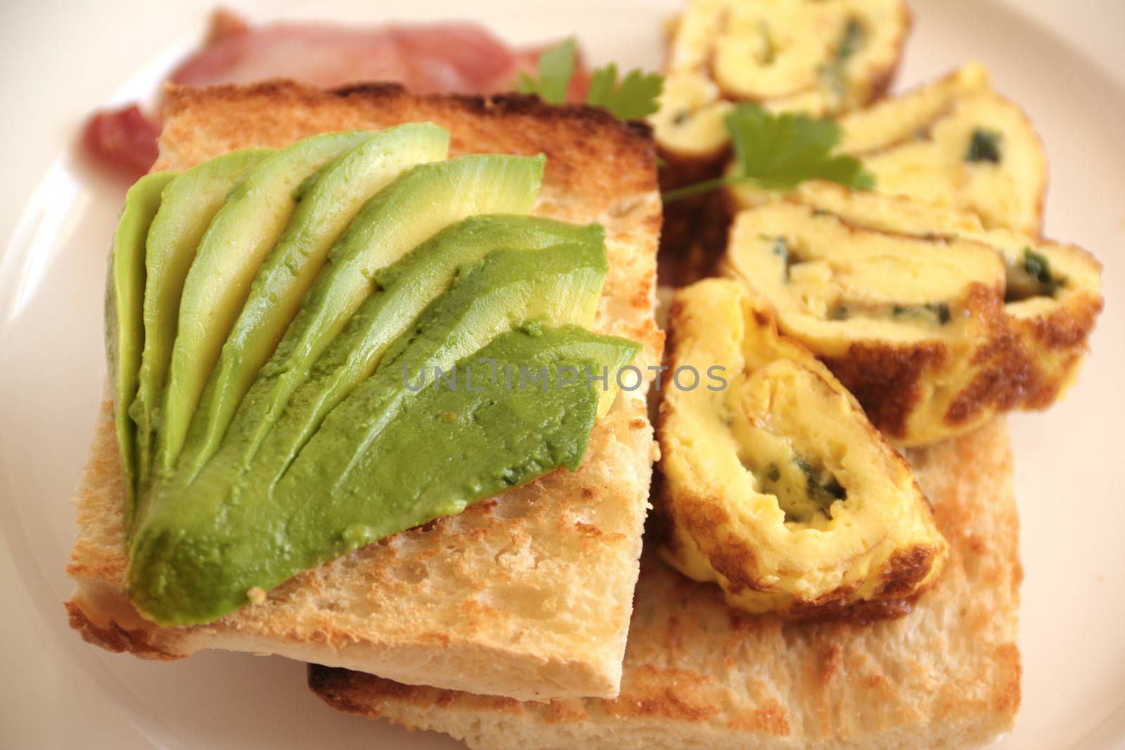 Sliced avocado on toasty Turkish bread with rolled omelette ready to serve.