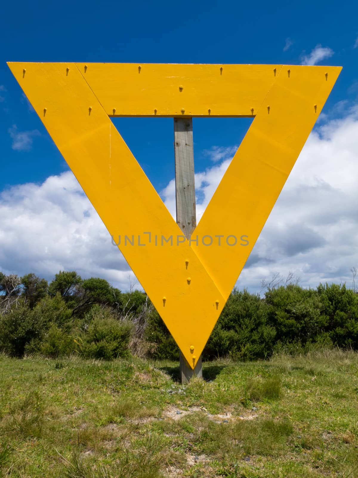 Strange yellow triangle sign on wooden post in coastal countryside landscape used as landmark orientation for shipping navigation