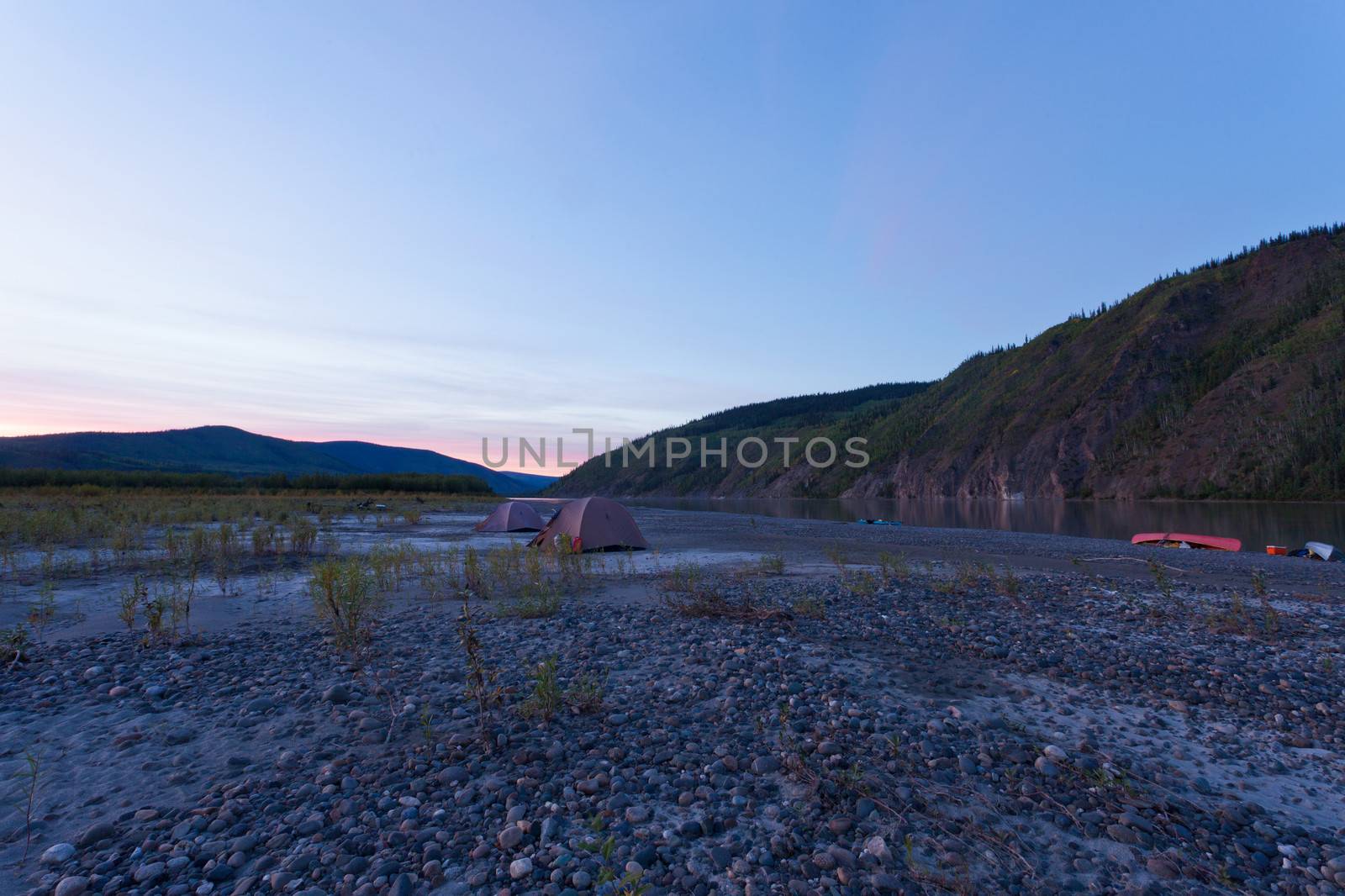 Midsummer night tent camp and beached canoes on Yukon River, Yukon Territory, Canada, in remote boreal forest wilderness