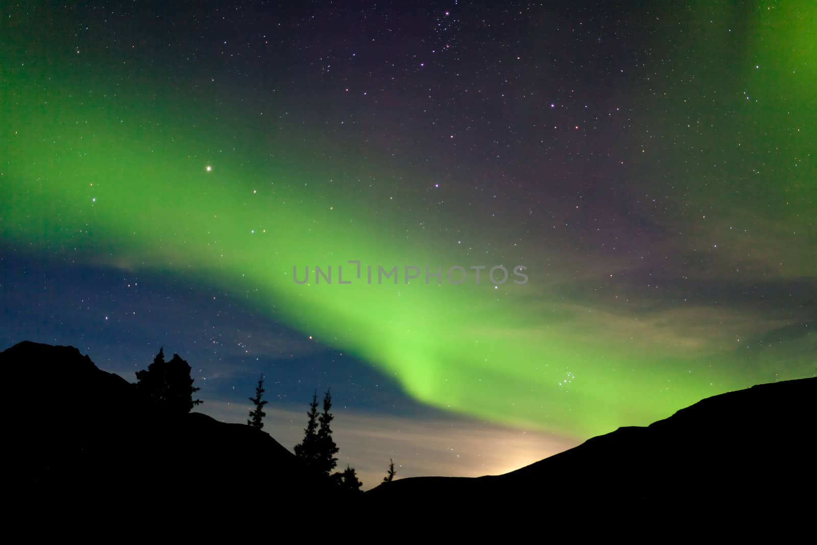 Intense bands of Northern lights or Aurora borealis or Polar lights dancing on night sky over hills with light glowing from moon rising behind them,Yukon Territory, Canada