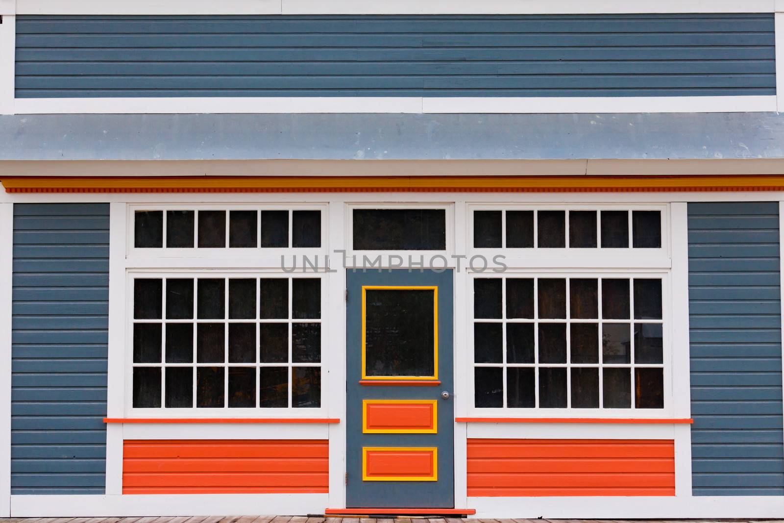 Symmetrical view of the front door and entrance to a quaint colorful wooden house with large cottage pane windows on either side