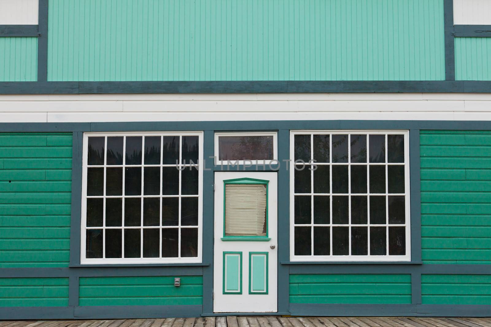 Symmetrical view of the front door and entrance to a quaint green wooden house with large cottage pane windows on either side