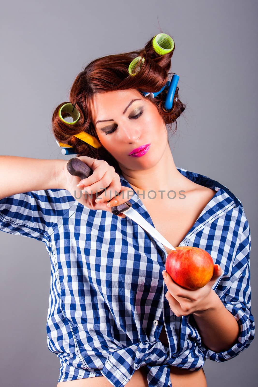 portrait of beautiful housewife with curlers holding apple and the knife