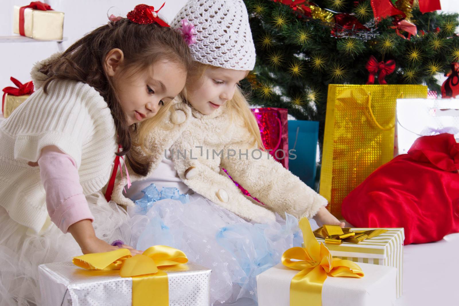 Two lovely little girls with presents under Christmas tree