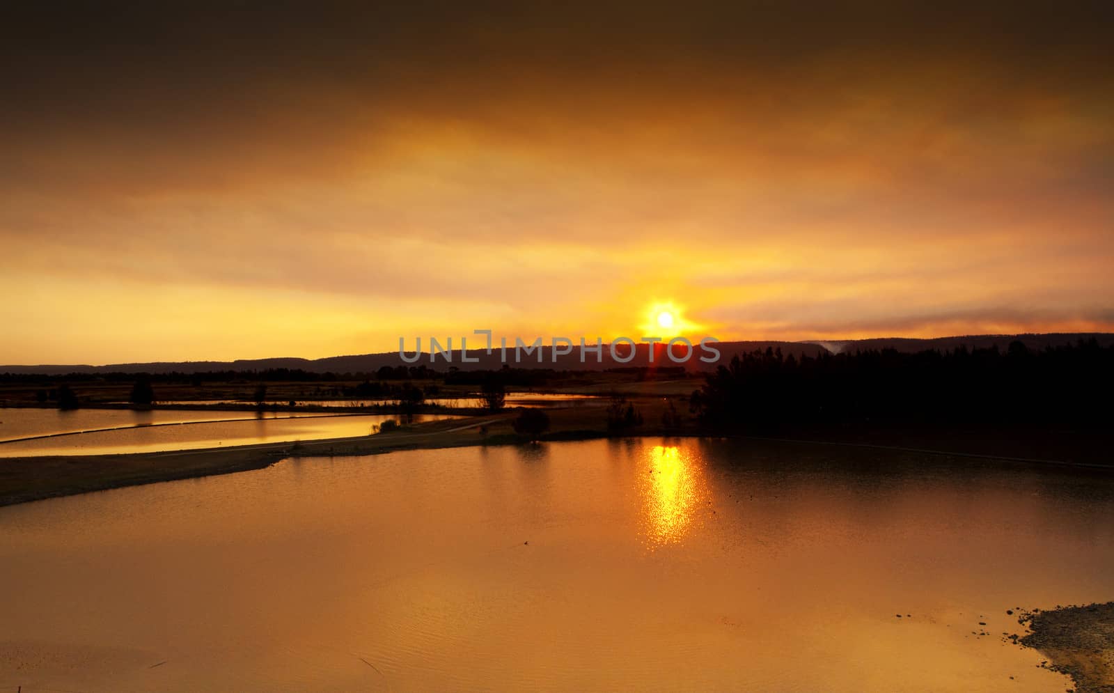 Sunset over Penrith Lakes. Ducks swim in the serene lakes as the warm golden orange sun sets behind the mountains.  Buyers, image has fine grain.