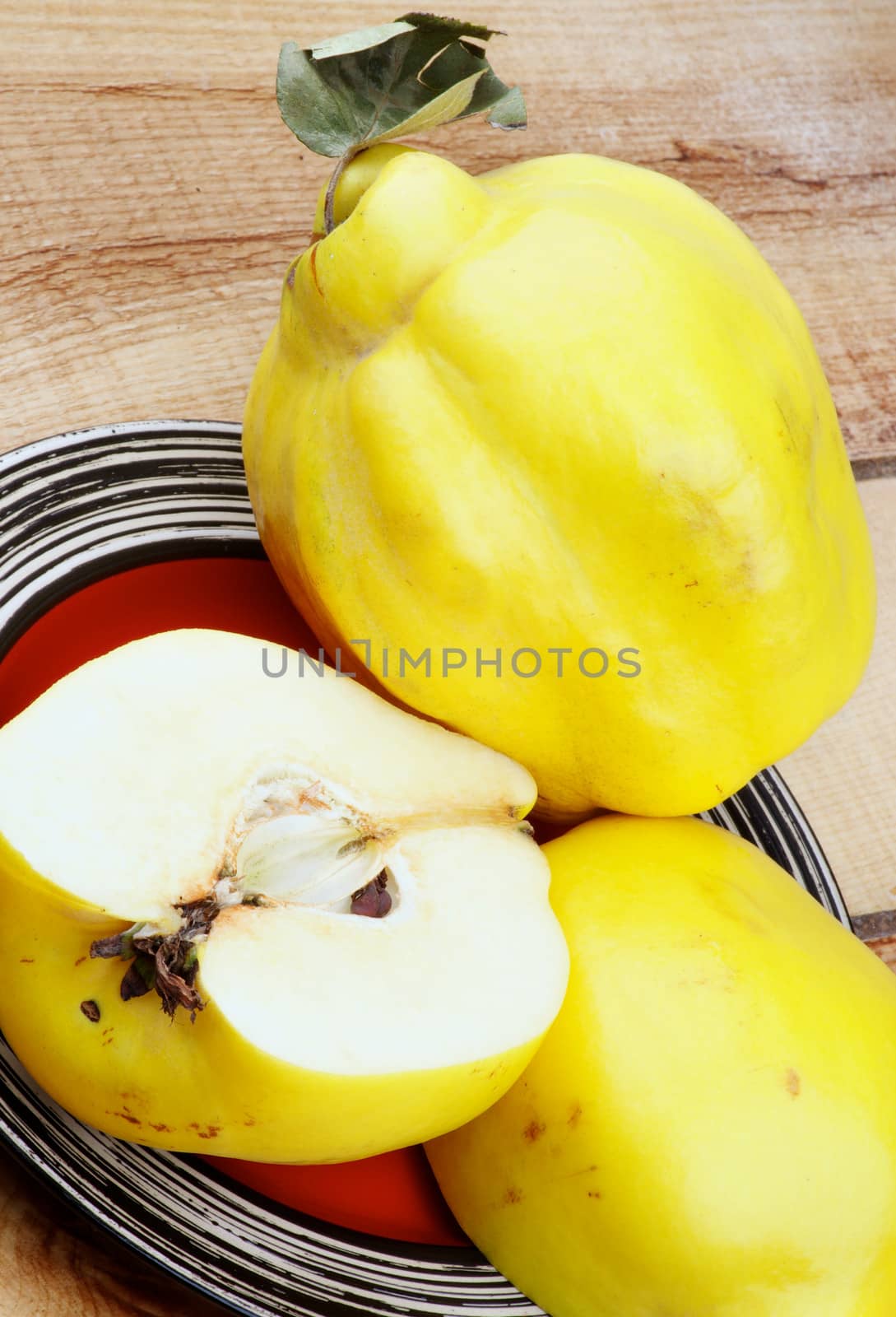 Arrangement of Delicious Big Ripe Quinces Full Body and Halves closeup on Striped Red Plate on Wooden background