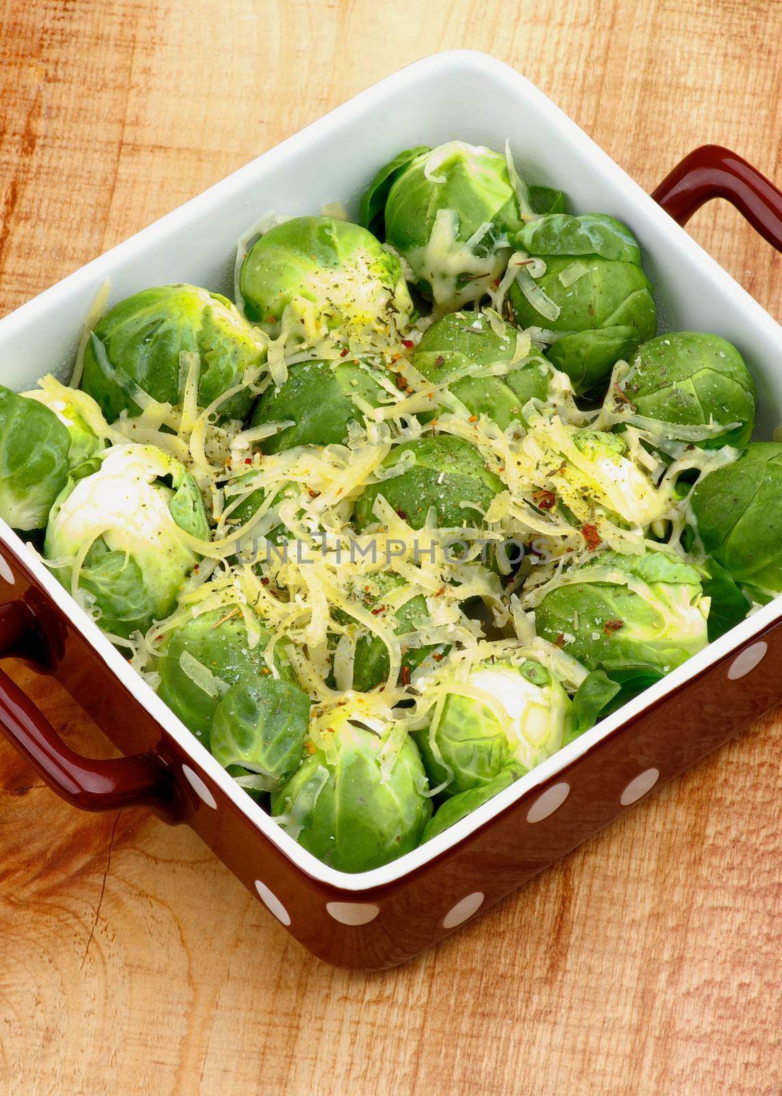 Brussels Sprouts Casserole in Brown Polka Dot Bowl with Grated Cheese and Spices closeup on Wooden background