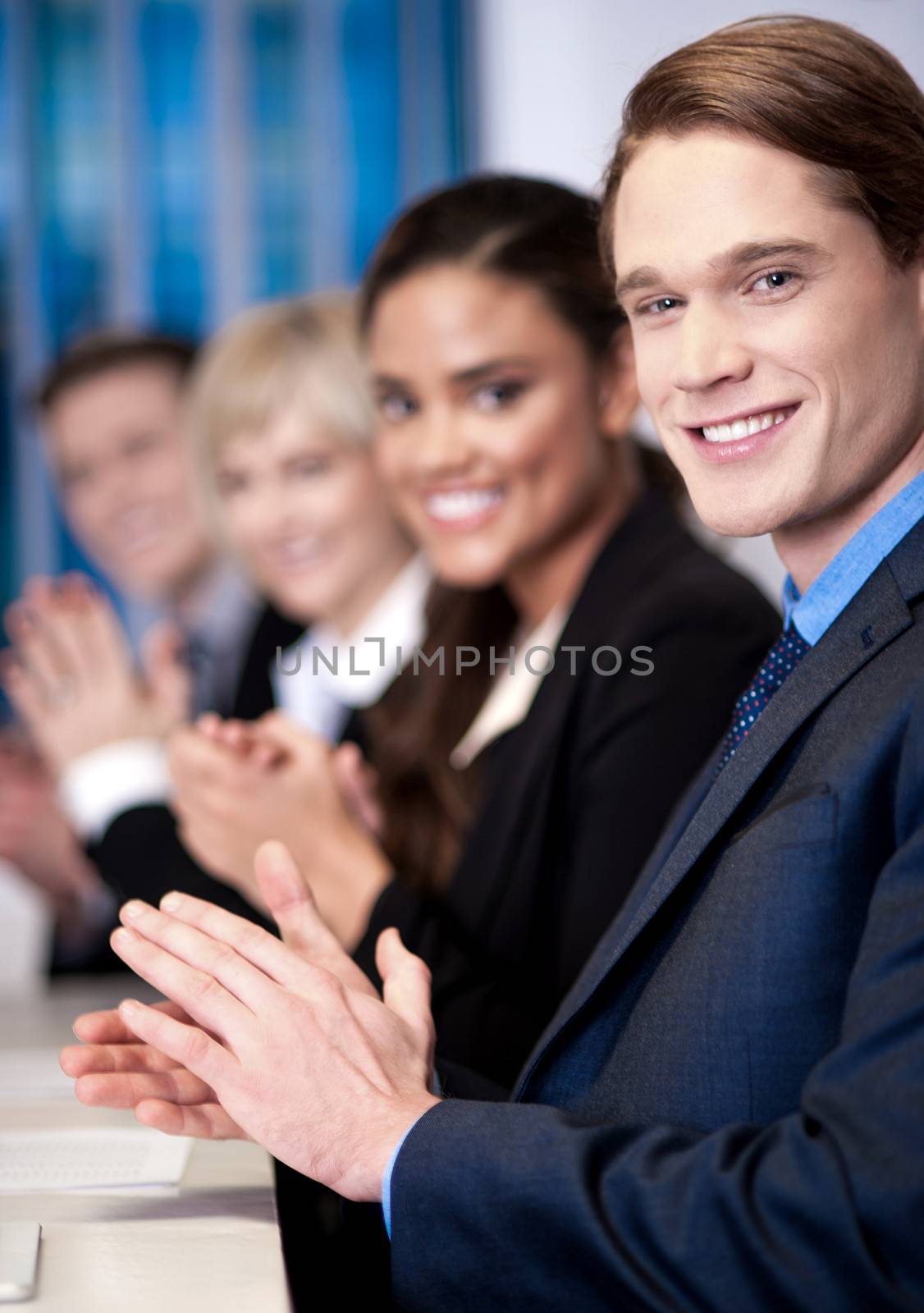 Corporate team sitting in a row and applauding by stockyimages