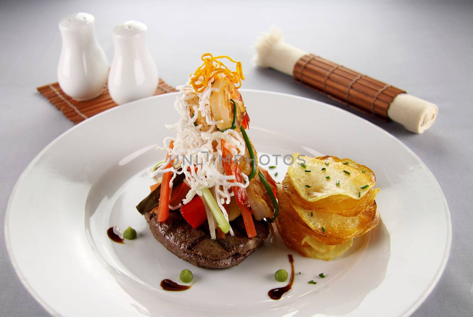 Delicious chargrilled steak with grilled shrimps, vegetables and potato chip stack.