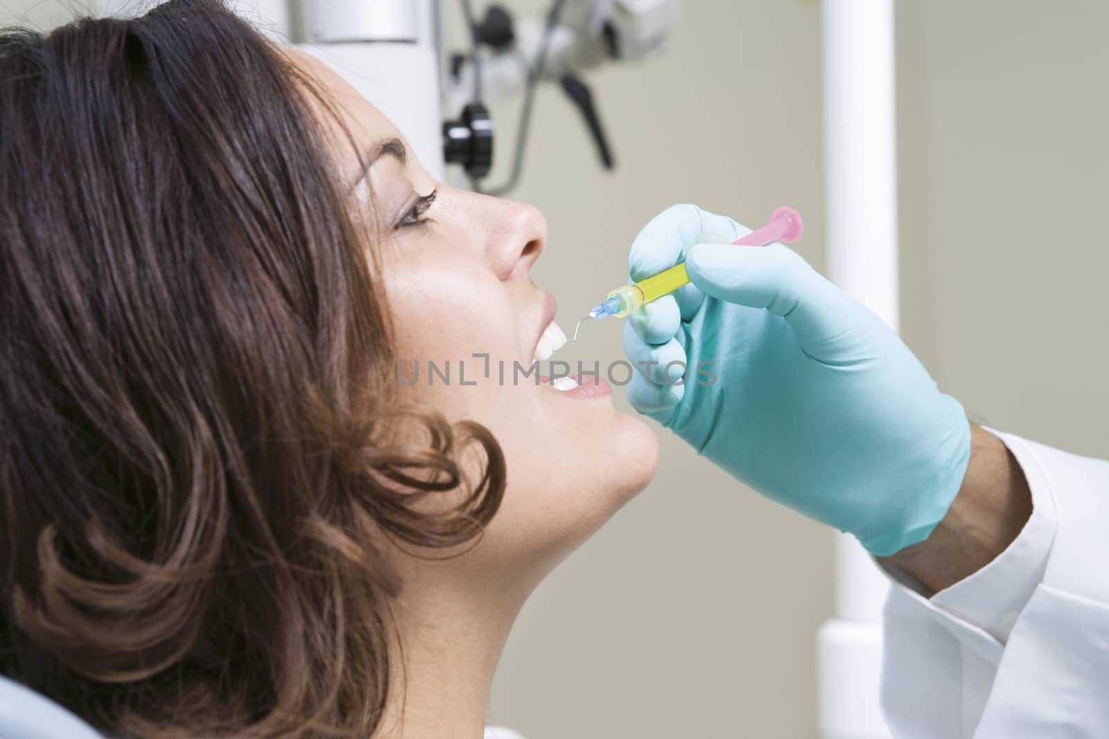 Dentist injecting female patient's teeth in clinic by moodboard