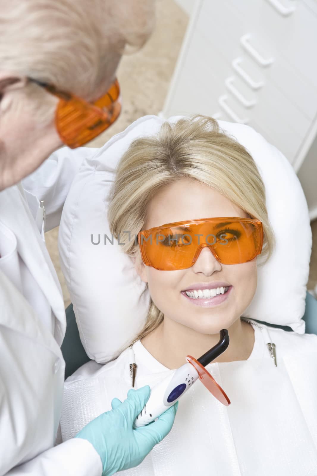 Dentist inspecting female patient's teeth using dental equipment in clinic by moodboard