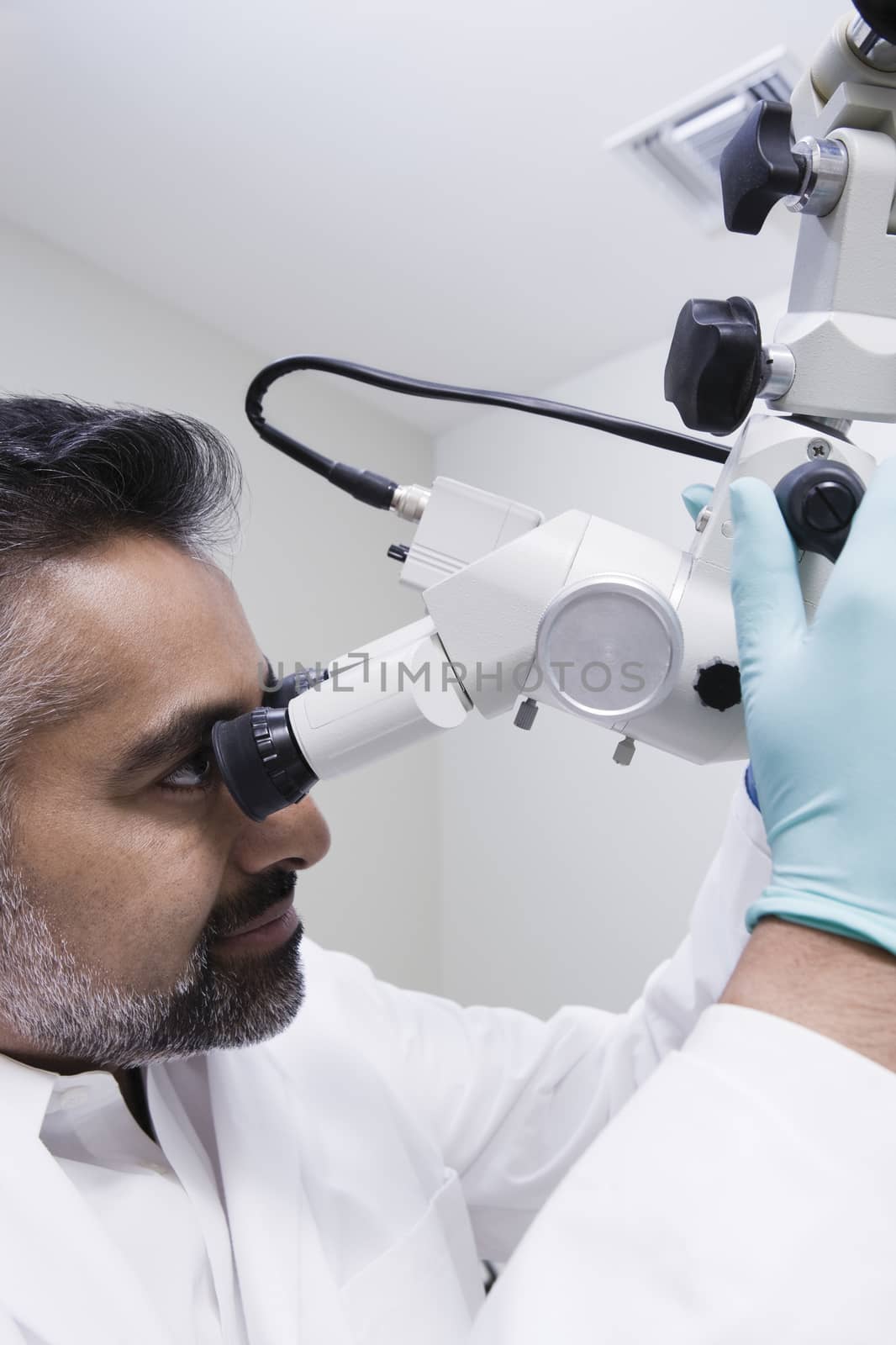 Closeup of an Asian male dentist using microscope in clinic by moodboard