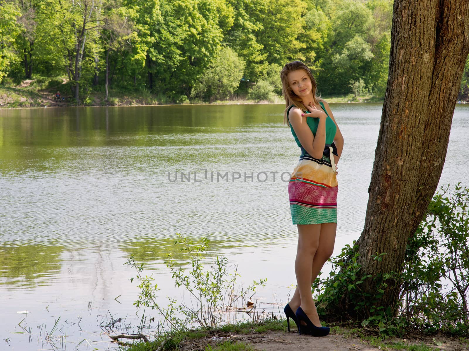 The young slender nice girl costs in a tree shadow in the sunny summer day