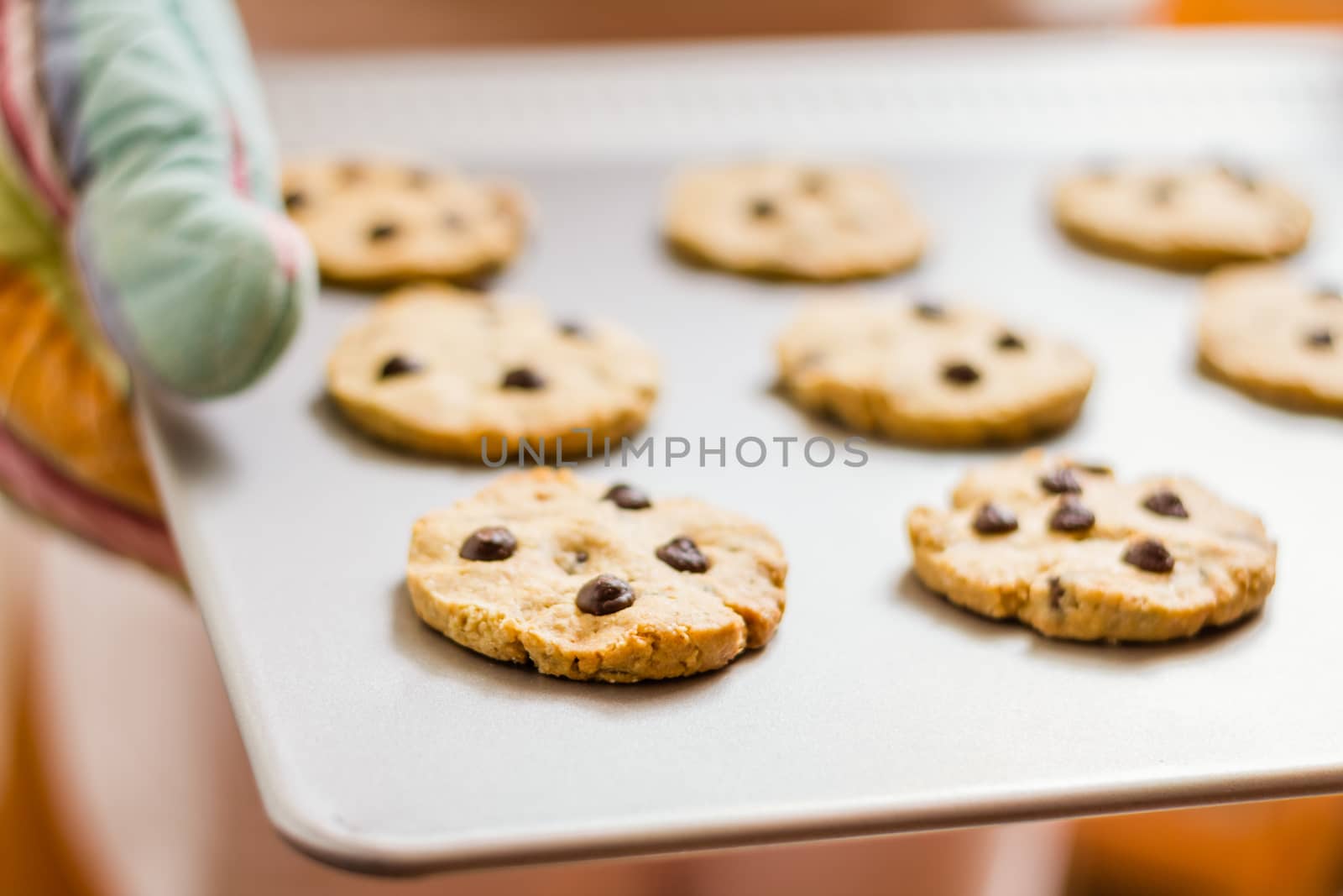 Woman holding a tray with baked cookies with kitchen gloves by doble.d