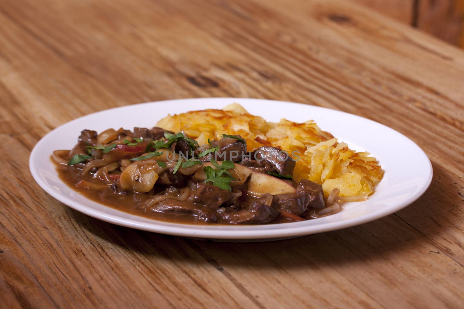 Venison goulash with apples and potatoes on plate with wooden background