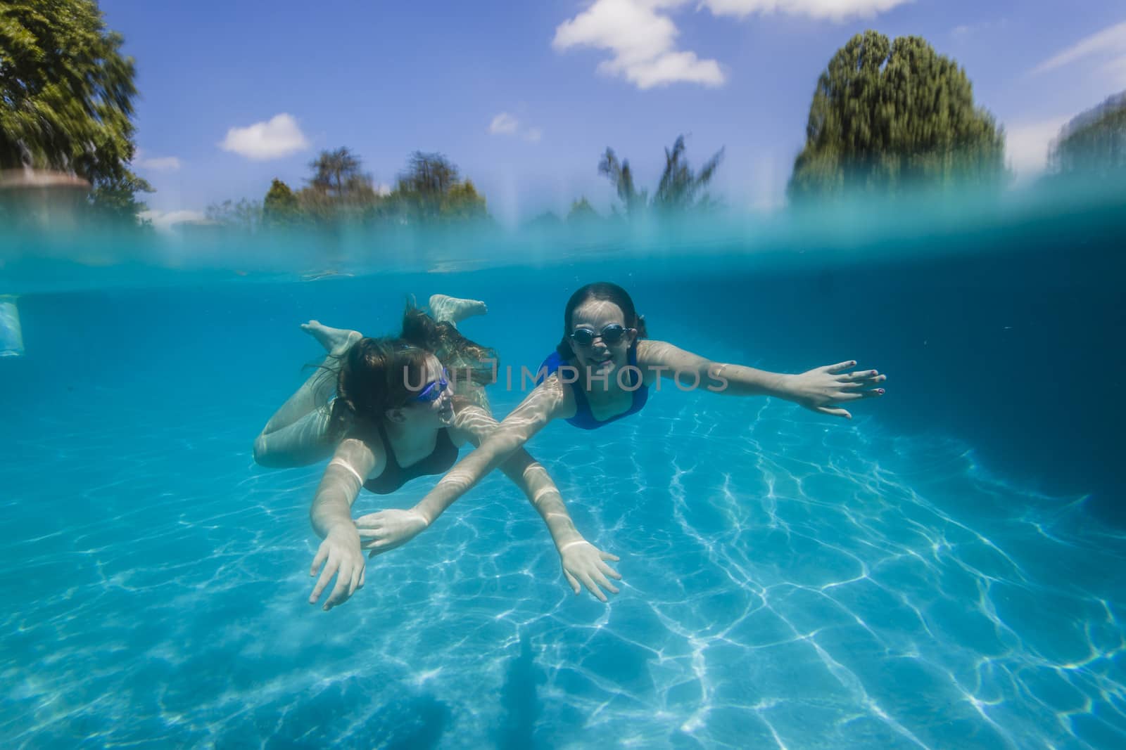 Young girls wearing training goggles swimming glide underwater together.