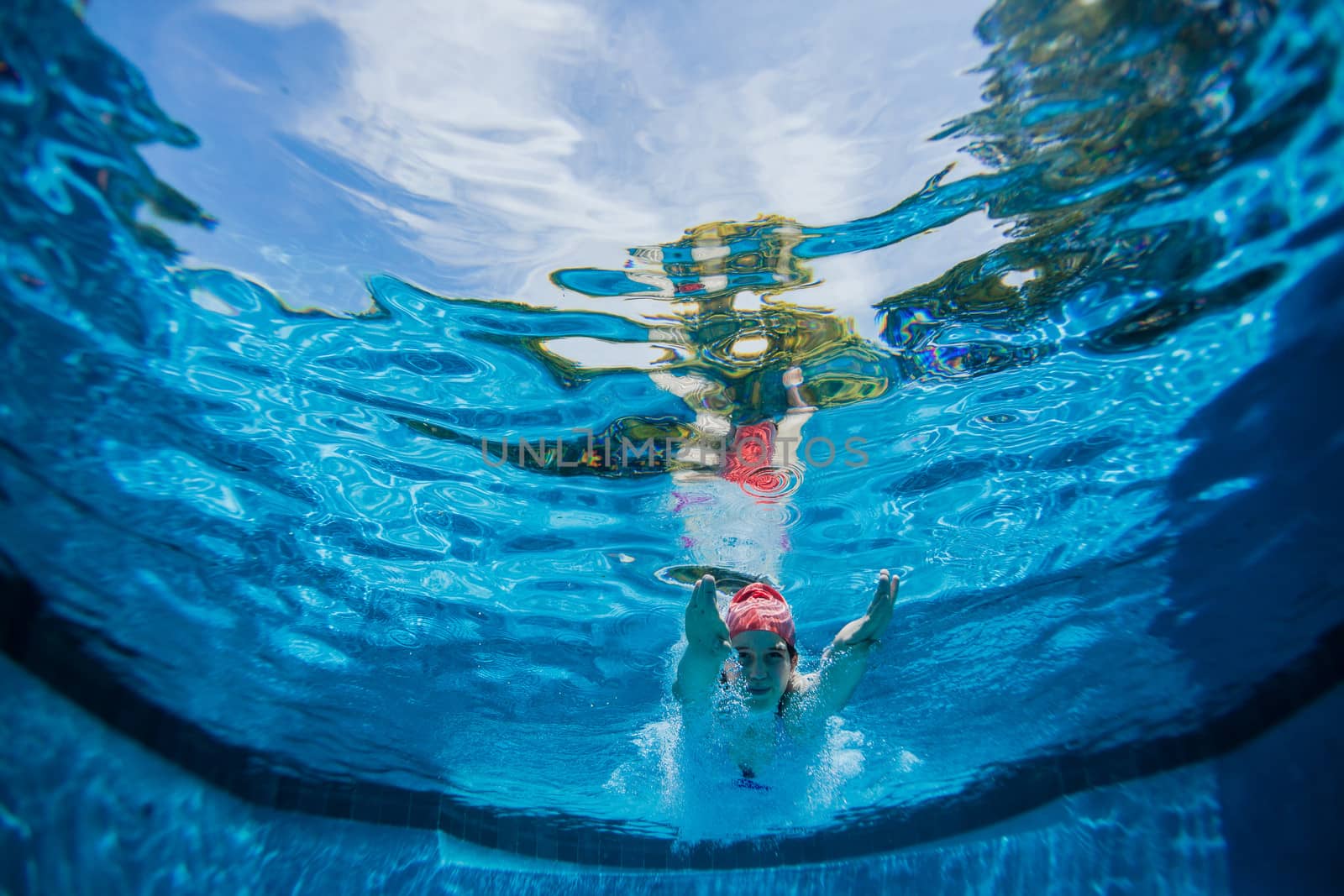 Young girl diving into swimming pool underwater towards lens.