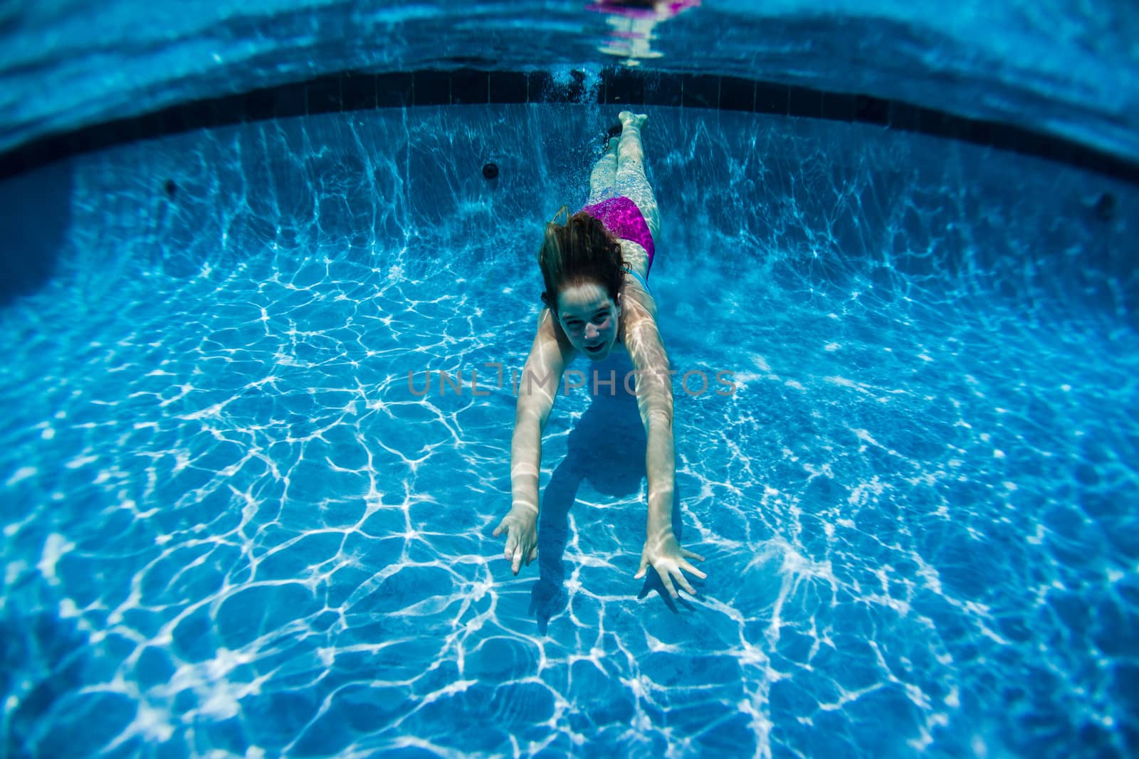 Young girl playtime glides underwater in outdoors home swimming pool
