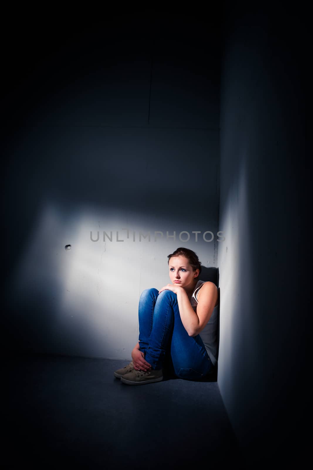 Young woman suffering from a severe depression (very harsh lighting is used on this shot to underline/convey the gloomy mood of the scene)